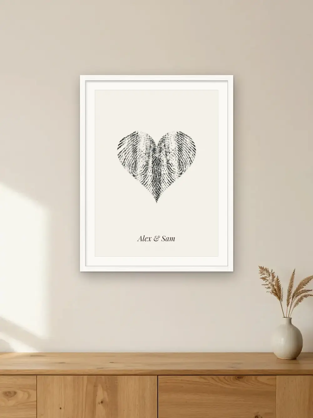 Anniversary gift mockup: a fingerprint heart made from two real ink prints, framed in white on a wall with the label “Alex & Sam · 10 years”