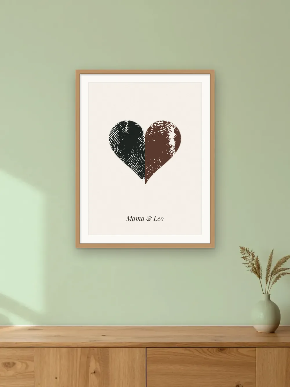Parent and child keepsake mockup: a fingerprint heart made from two real ink prints, in an oak frame on a sage nursery wall labelled “Mama & Leo”